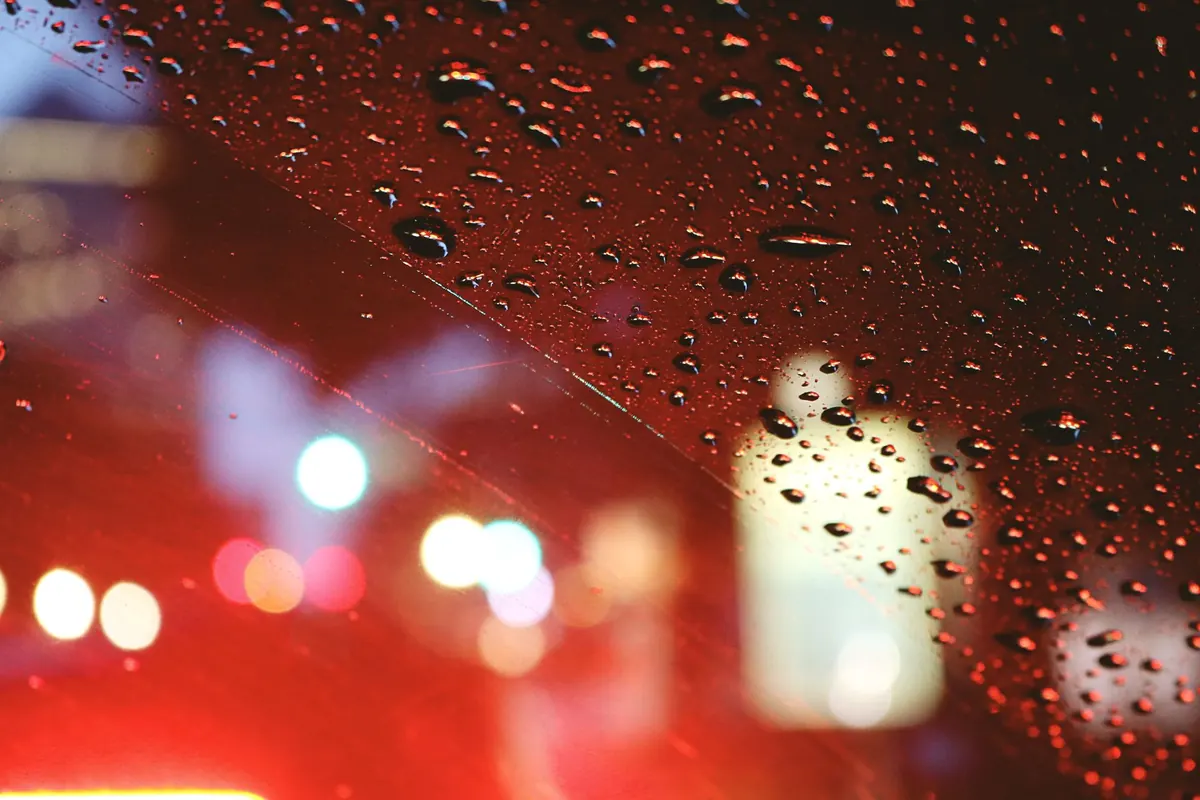 Gotas de chuva no vidro de um carro com luzes ao fundo