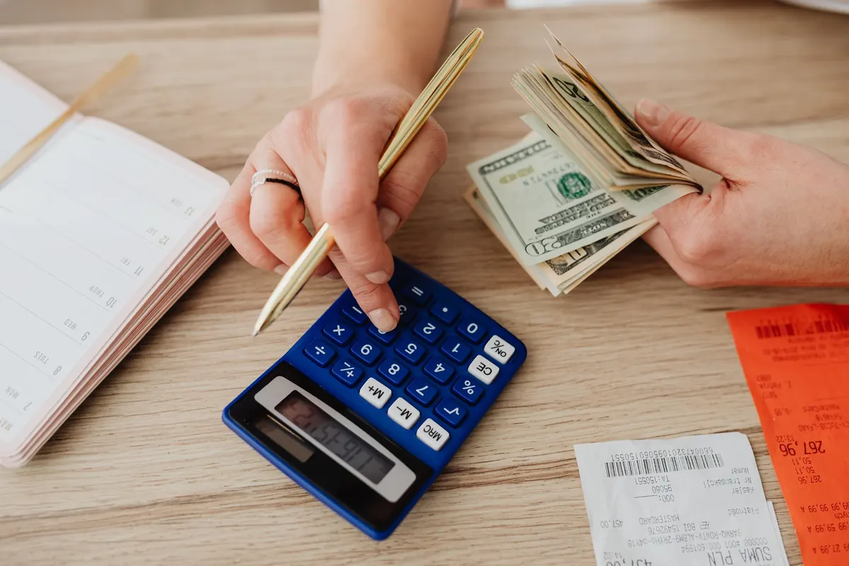 Mãos com dinheiro e calculadora planejando um orçamento