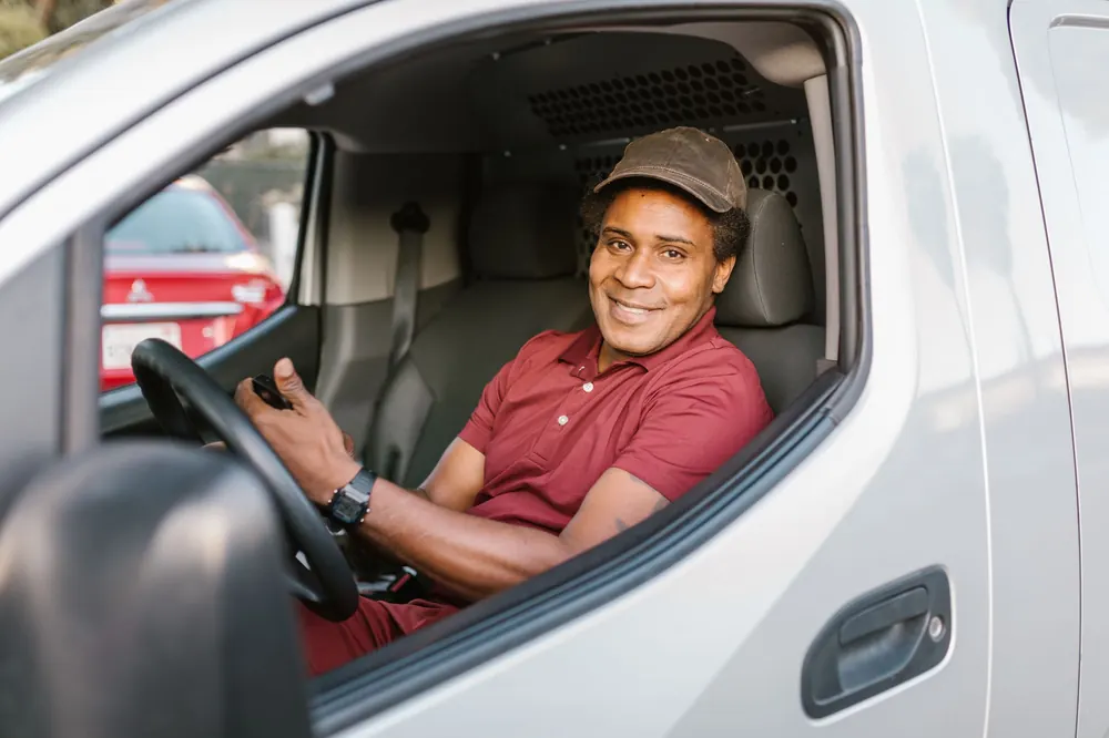 Motorista sorrindo dentro da van com o celular na mão